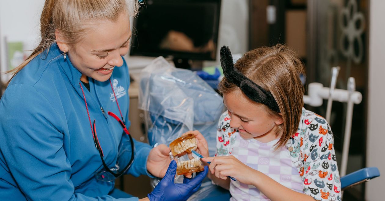 girl practice brushing with dental assistant and fake teeth